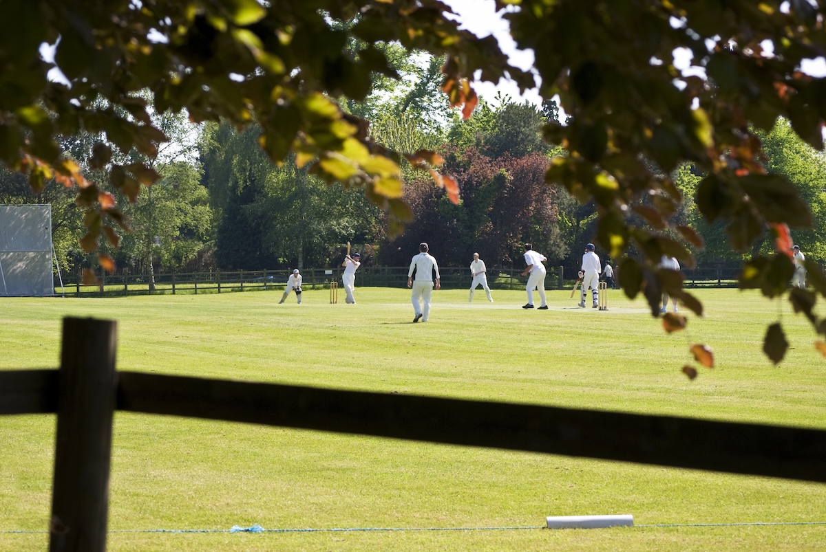 A game of cricket being played on a field surrounded by trees. 