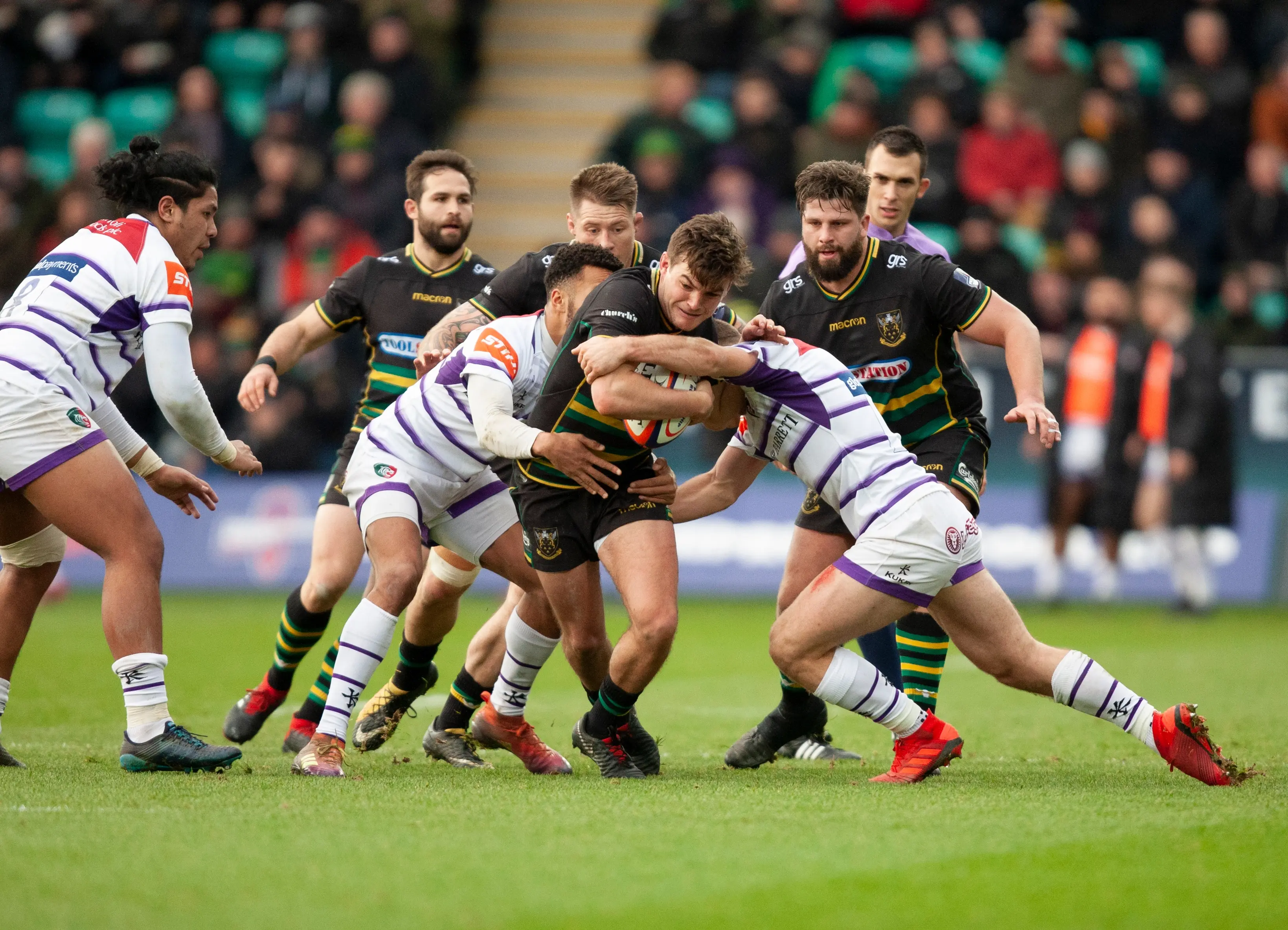 A rugby player carrying a rugby ball while being tackled by two players.