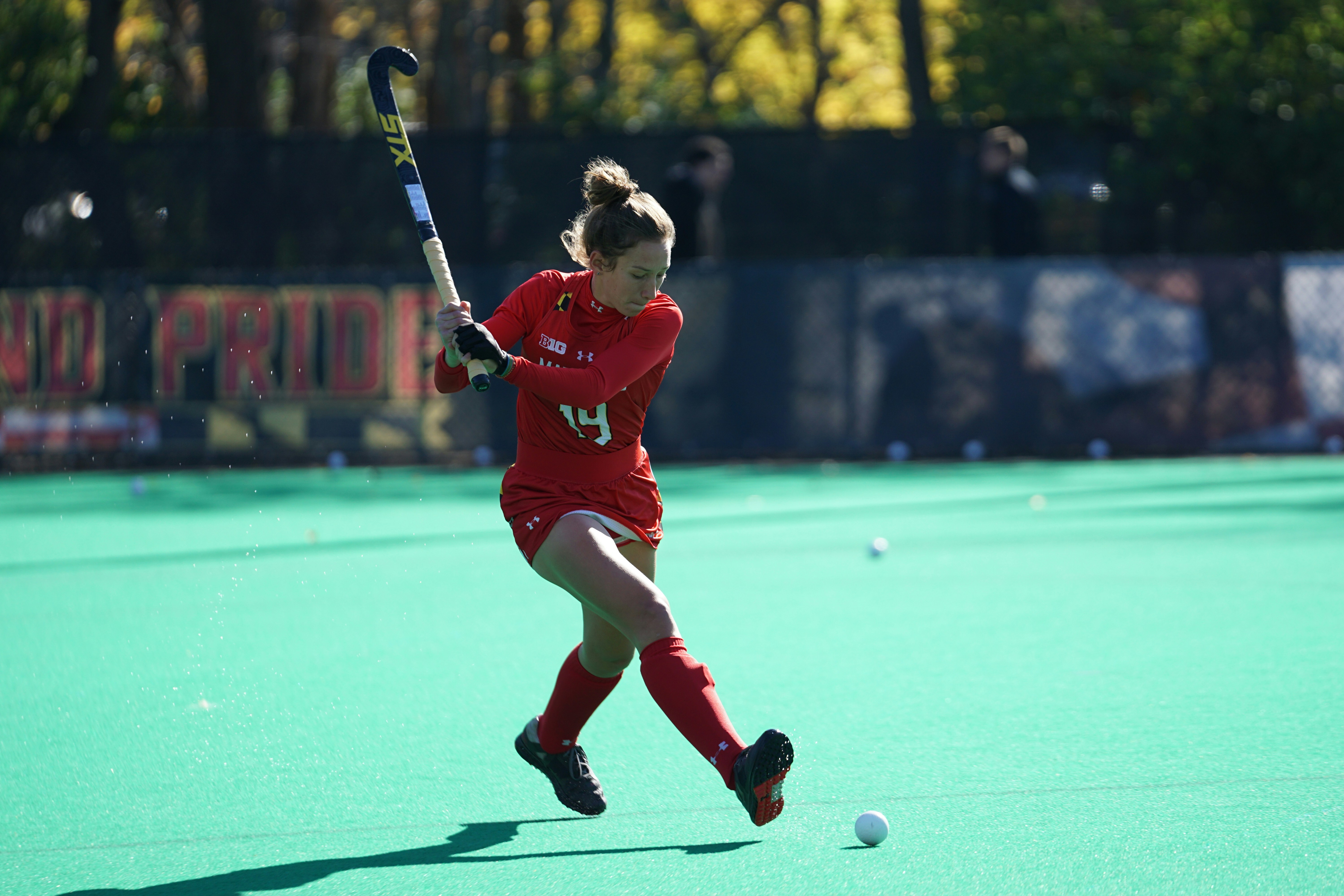 A field hockey player swinging her stick to hit a ball. 